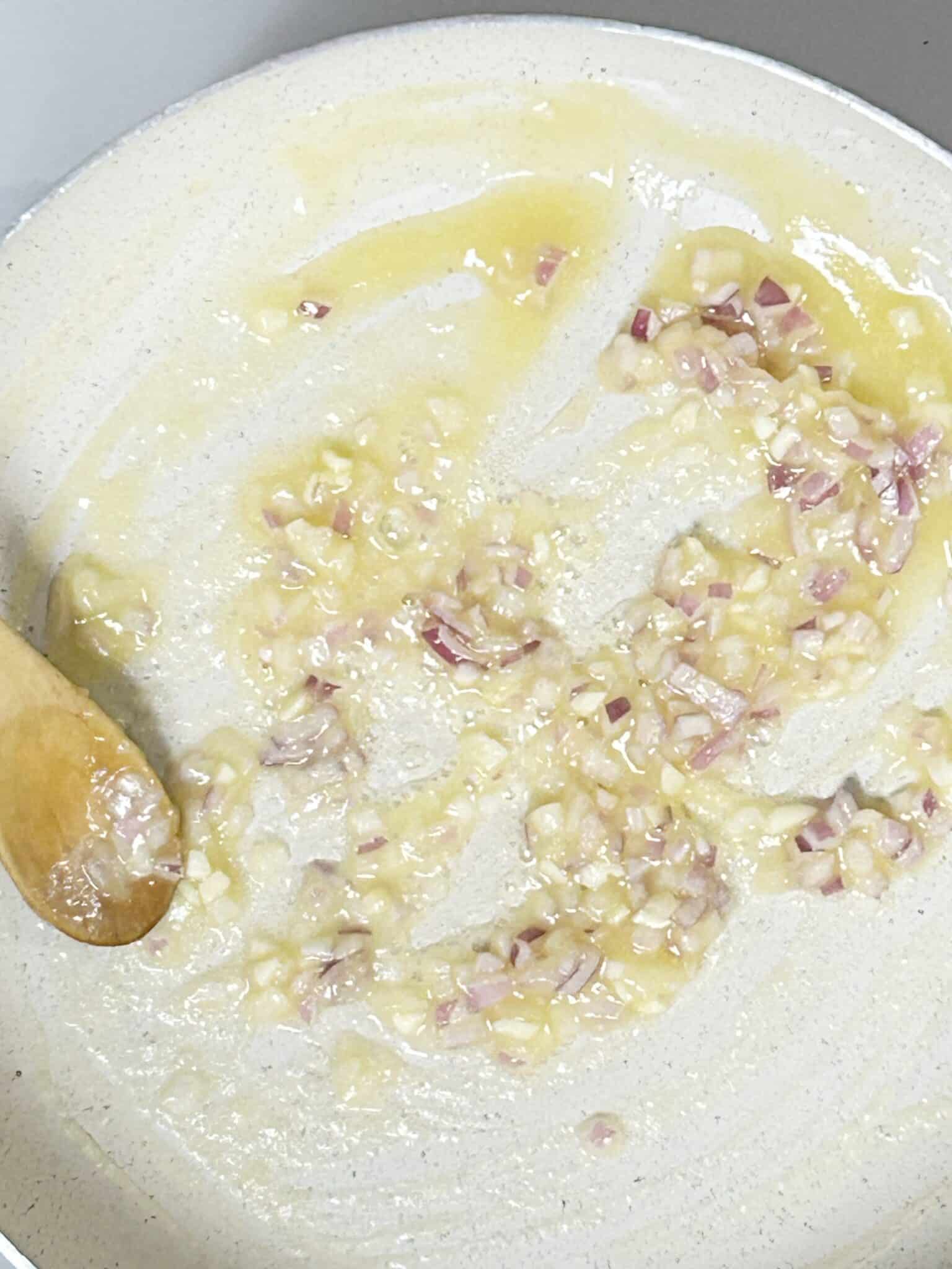 Minced garlic and shallots cooking in a pan until softened Minced garlic and shallots cooking in a pan until softened
