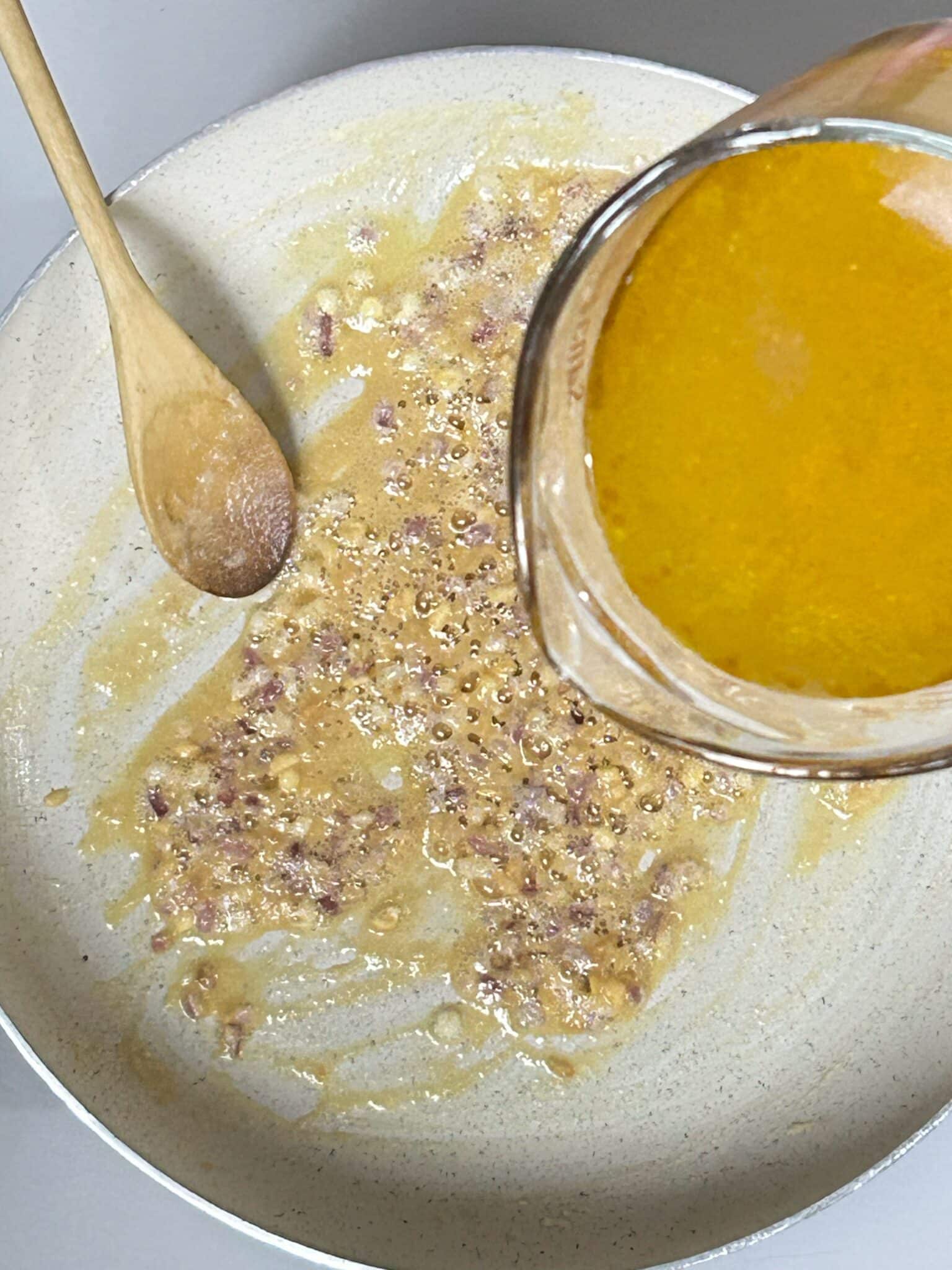 Whisking broth into the golden roux in a saucepan Whisking broth into the golden roux in a saucepan