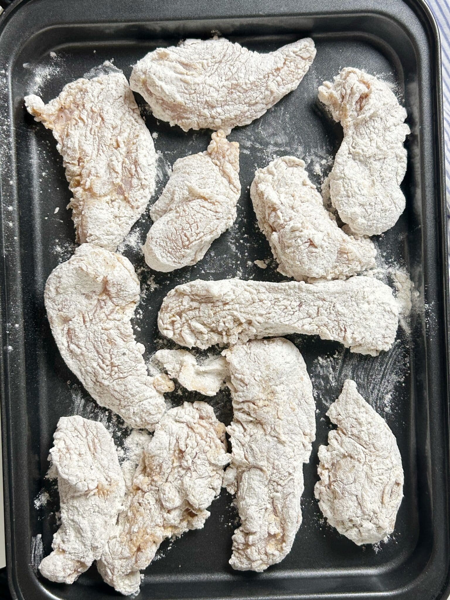 All chicken strips coated in flour mixture and arranged on a tray All chicken strips coated in flour mixture and arranged on a tray