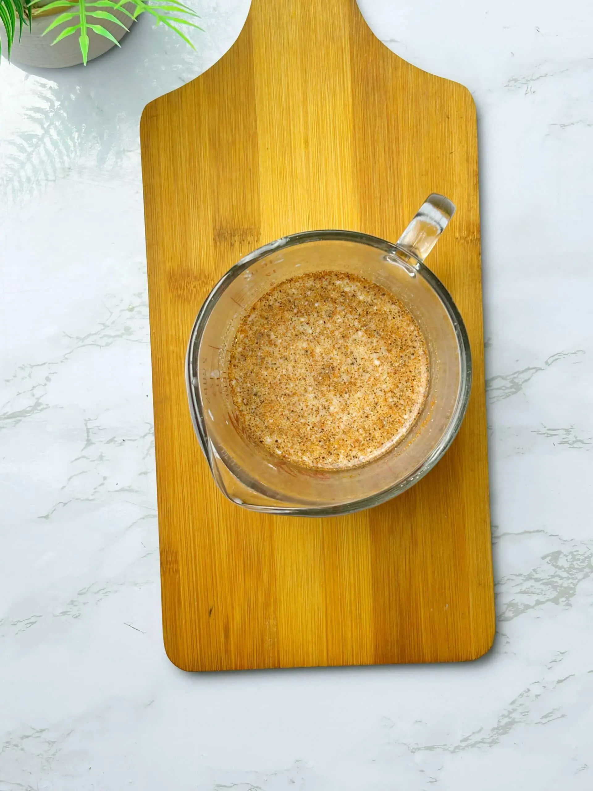 Seasoned buttermilk marinade with spices in a glass measuring cup on a wooden cutting board