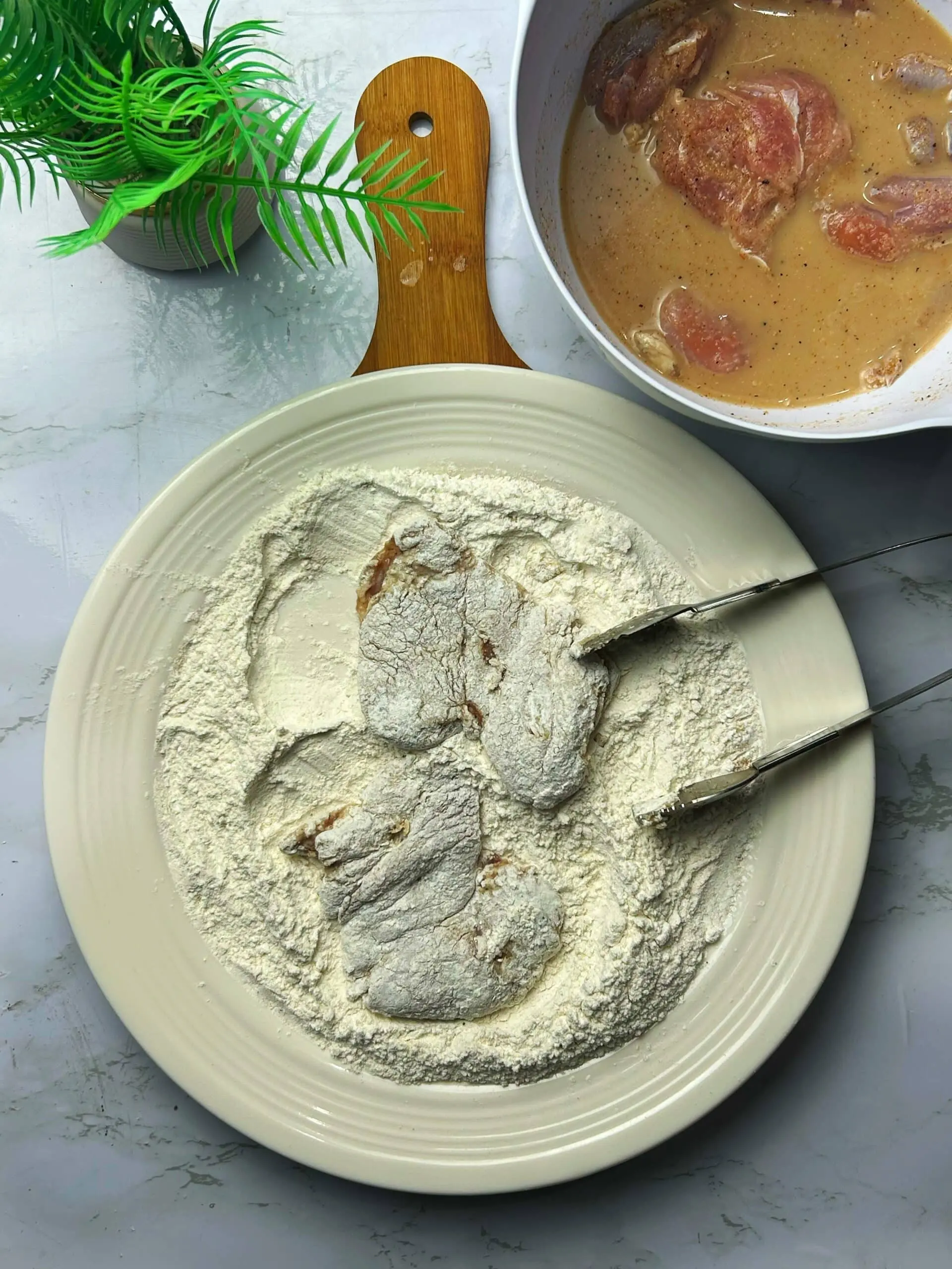 Chicken thighs being dredged in seasoned flour after marinating in buttermilk brine
