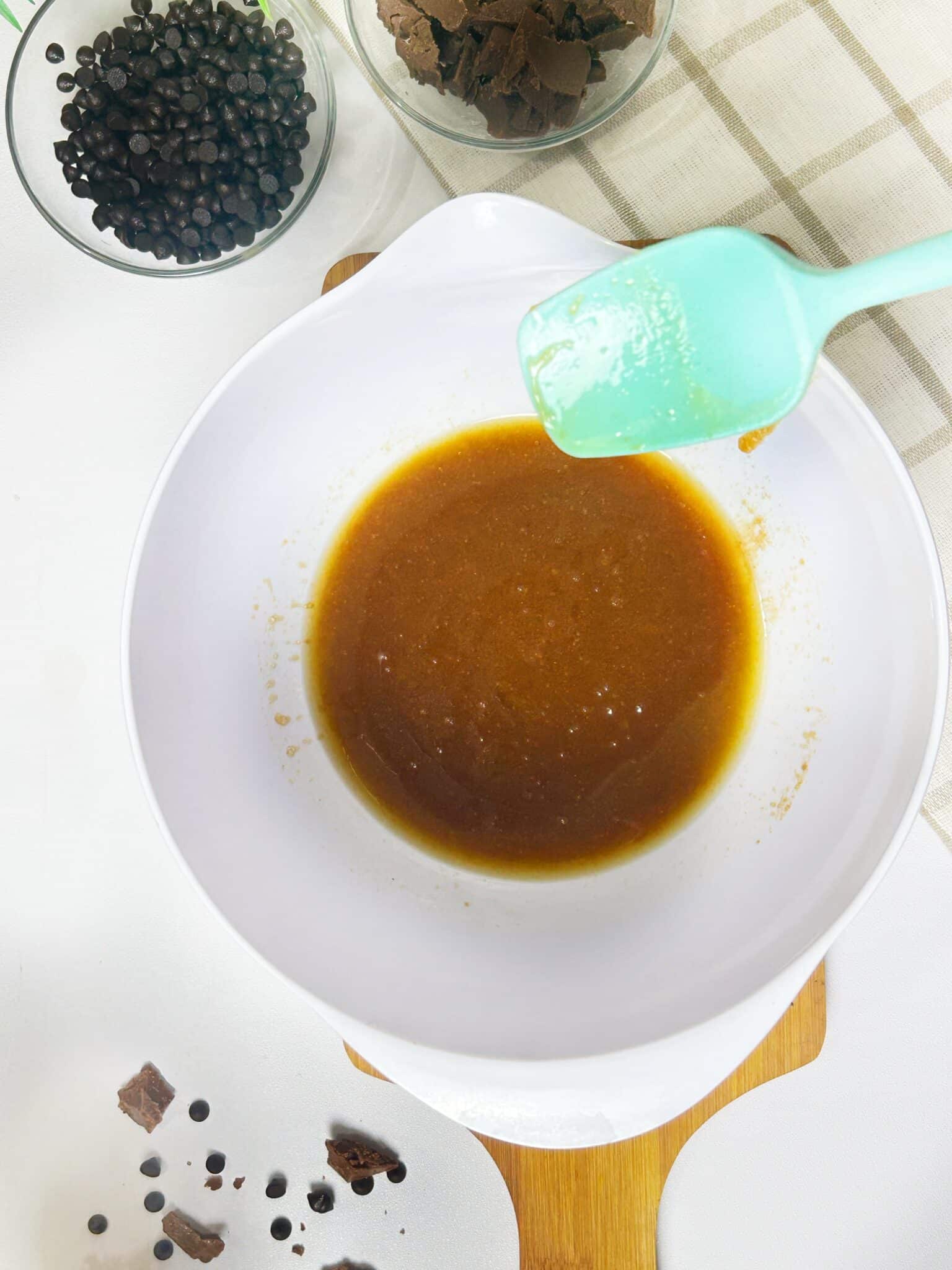 Mixing melted butter, sugar, egg, and vanilla in a bowl for chocolate chip cookie dough