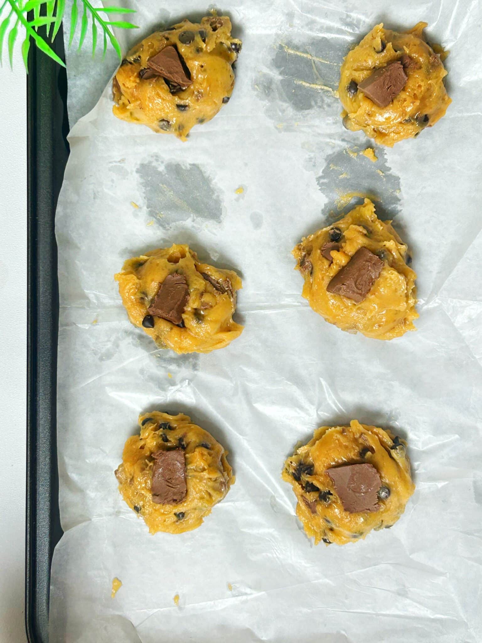 Scooping chocolate chip cookie dough into small balls and placing them on a baking tray with space between each